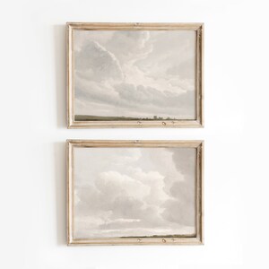 May include: Two framed landscape paintings with a light gray background and white clouds. The top painting shows a field with a small town in the distance. The bottom painting shows a field with a cloudy sky.