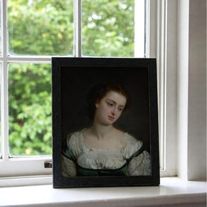 May include: A framed portrait of a woman with brown hair and a white lace collar. She is wearing a green dress and has a blue flower in her hair. The portrait is set against a dark background.