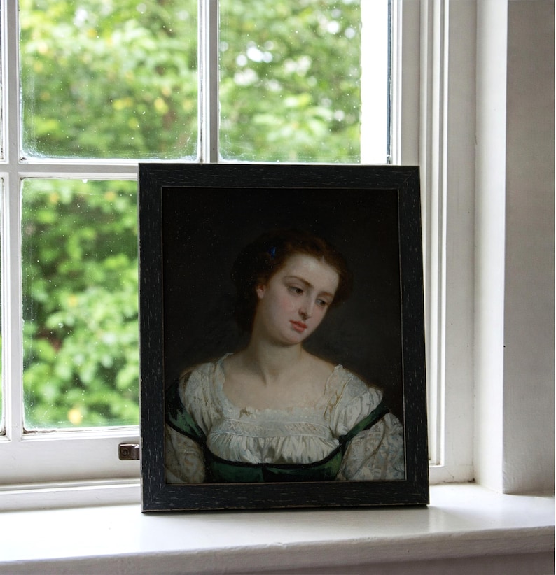 May include: A framed portrait of a woman with brown hair and a white lace collar. She is wearing a green dress and has a blue flower in her hair. The portrait is set against a dark background.