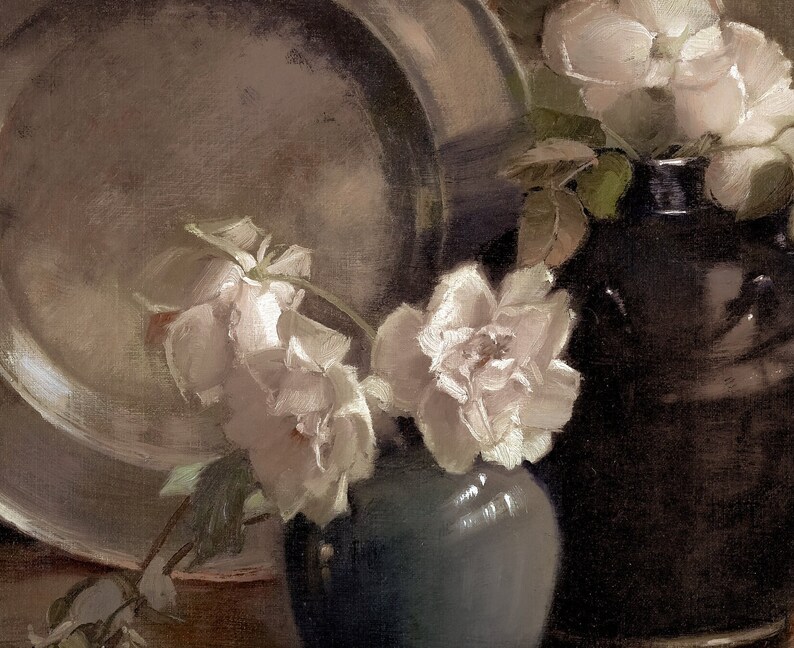K&ouml;nnte beinhalten: Ein Stillleben mit wei&szlig;en Rosen in einer blauen Vase, im Hintergrund ein silbernes Tablett und eine dunkelbraune Keramikvase.