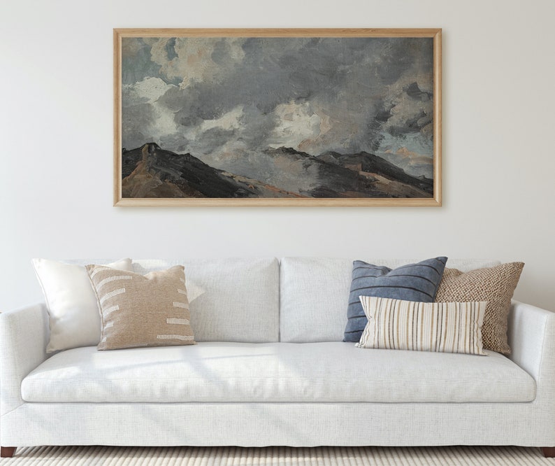 May include: A white sofa with a framed painting of a mountain landscape with a cloudy sky above. The sofa has three cushions, one blue, one beige, and one with a striped pattern.
