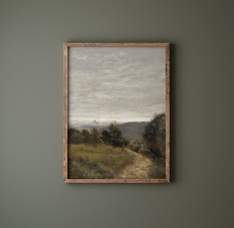 May include: A framed painting depicting a landscape scene with a winding path leading through a field of green grass and trees. The sky is a muted gray with a few wispy clouds.