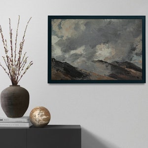 May include: A framed painting depicting a landscape with a cloudy sky and rolling hills. The sky is a mixture of grey and white, with glimpses of blue. The hills are a dark brown, with some areas of green and yellow. The painting is framed in a dark wood frame.