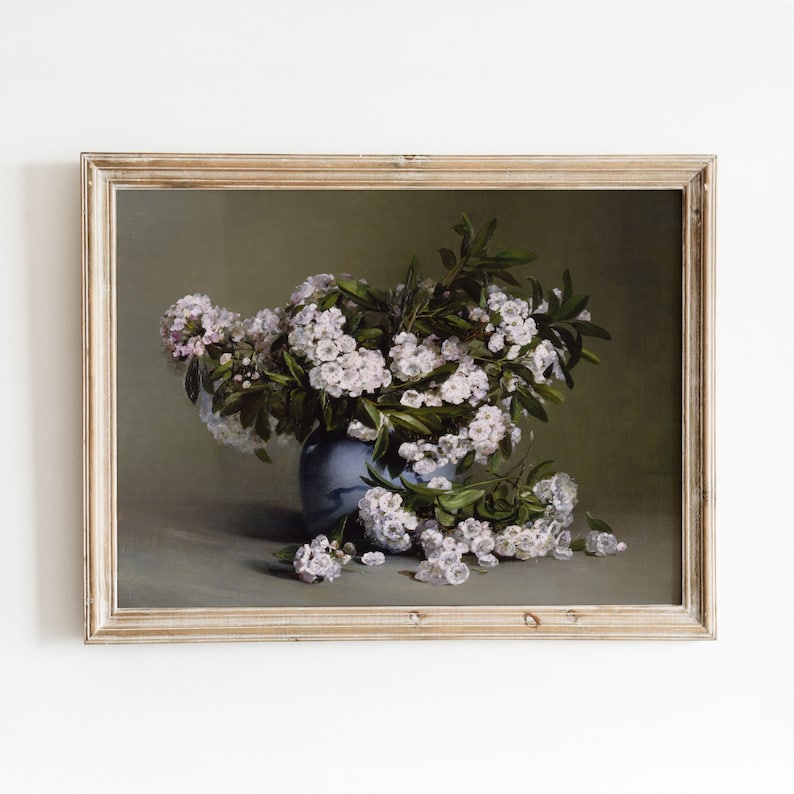 May include: A framed painting of a bouquet of white flowers in a blue vase. The flowers are arranged in a vase on a table with a green background.