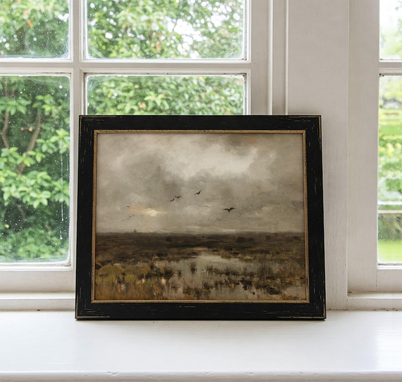 May include: A framed painting depicting a landscape with a cloudy sky and a flock of birds flying over a marsh. The painting is in a black frame with a gold inner border.