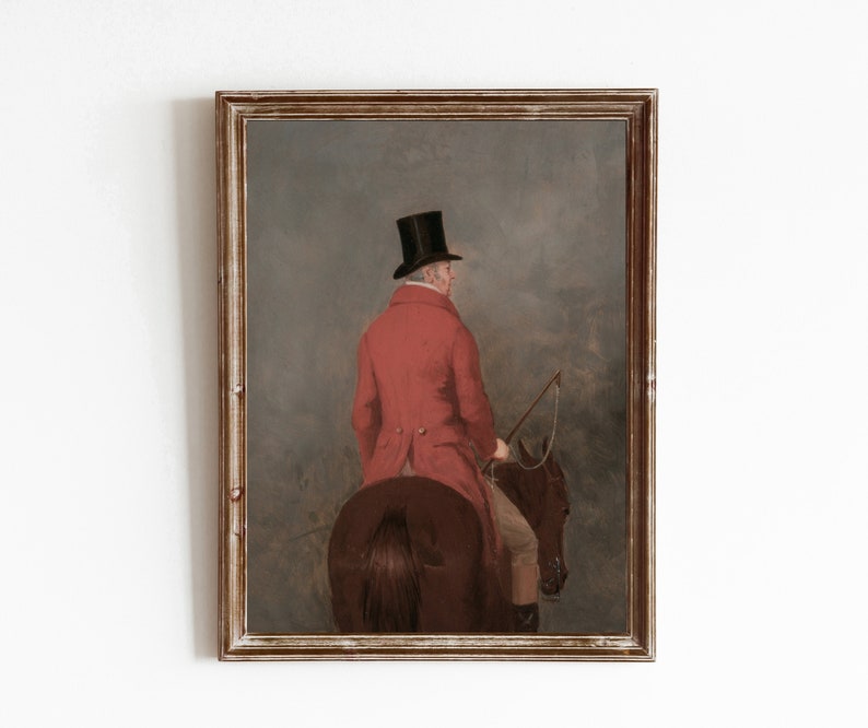 May include: A framed oil painting depicting a man in a red coat and black top hat riding a brown horse. The man is facing away from the viewer and holding a riding crop. The background is a hazy landscape.