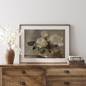 May include: A framed print of a still life painting featuring a bouquet of white roses in a vase. The roses are arranged in a loose, natural style, and the vase is a simple, elegant design. The background is a soft, muted color.