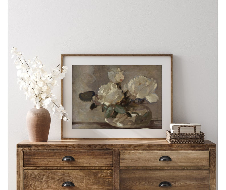 May include: A framed print of a still life painting featuring a bouquet of white roses in a vase. The roses are arranged in a loose, natural style, and the vase is a simple, elegant design. The background is a soft, muted color.