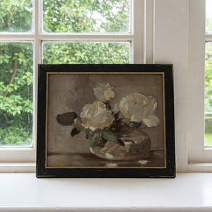 May include: A framed painting of white flowers in a clear glass vase. The flowers are arranged in a loose, natural style, and the painting is done in a realistic style.