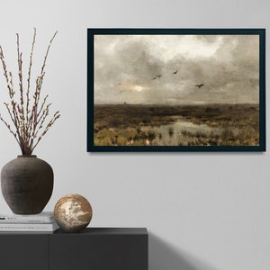 May include: A framed painting depicting a landscape with a cloudy sky and a flock of birds flying over a marsh. The painting is in a black frame and is hanging on a white wall.