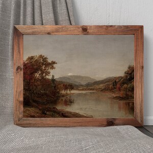 K&ouml;nnte beinhalten: Gerahmtes Landschaftsgem&auml;lde mit einer ruhigen Seeszene und Bergen im Hintergrund. Das Kunstwerk zeigt Herbstlaub in Rot- und Braunt&ouml;nen unter einem bew&ouml;lkten Himmel. Der Holzrahmen verleiht einen rustikalen Touch.