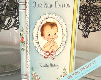 May include: Vintage baby-themed family history book with a light blue cover. The cover features a baby illustration within a white lace oval, the text "Our New Edition" and "Family History". The spine is light blue with pink floral accents.