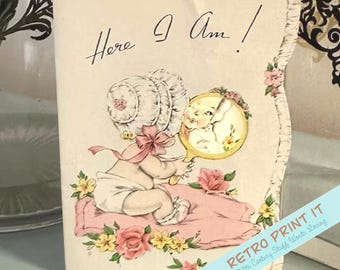 May include: Vintage greeting card featuring a baby in a bonnet looking in a mirror. The card has the text "Here I Am!" in script. The baby is sitting on a pink pillow surrounded by pink and yellow flowers. The card has a scalloped edge.