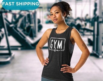 Puede incluir: Una camiseta sin mangas gris oscuro con las palabras "GYM life" en un marco rectangular blanco. La persona lleva leggings grises y está en un gimnasio.