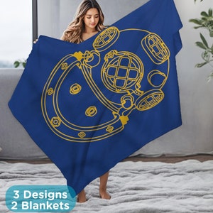 May include: A blue blanket with a gold outline of a diving helmet. The blanket is being held by a person.