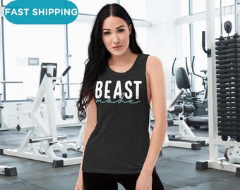 Puede incluir: Un top de tirantes negro con el texto "BEAST MODE" en blanco con un subrayado azul turquesa. El top de tirantes lo lleva puesto una persona en un entorno de gimnasio.