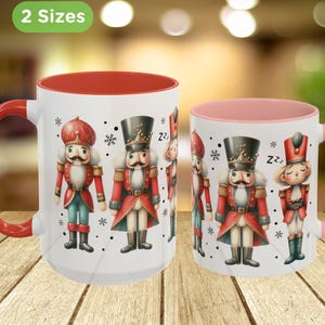 May include: Two white ceramic mugs with red and pink interiors and handles. The mugs feature illustrations of toy nutcrackers in red, black, and blue uniforms. The text "2 Sizes" is in a green oval.