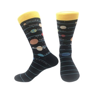 Peut inclure: Une paire de chaussettes noires avec un bord jaune. Les chaussettes présentent un motif coloré du système solaire, avec des planètes étiquetées et disposées le long de lignes bleues. Un accessoire amusant et éducatif.