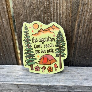 May include: A camping-themed sticker with a tent, trees, mountains, sun, and the text "the algorithm can't reach me out here". The sticker is in shades of green, brown, orange, and pink.