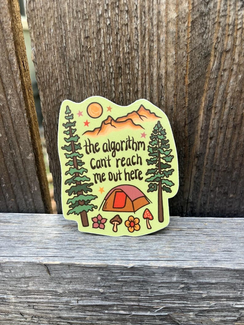 May include: A camping-themed sticker with a tent, trees, mountains, sun, and the text "the algorithm can't reach me out here". The sticker is in shades of green, brown, orange, and pink.