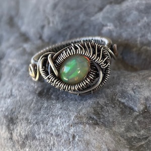 May include: A silver wire wrapped ring with a green opal gemstone. The ring is handmade and features a unique design.