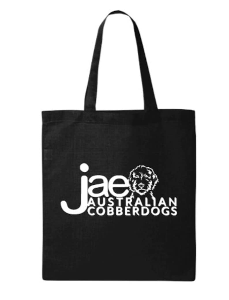 Puede incluir: Bolso tote negro con texto blanco e ilustraci&oacute;n de perro. El texto dice "jae AUSTRALIAN COBBERDOGS". El bolso tiene dos asas largas para llevar al hombro.