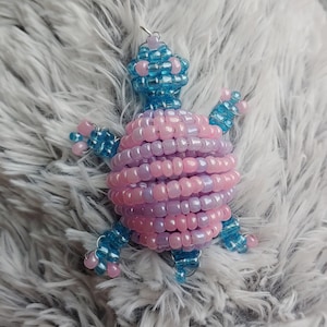 May include: A beaded turtle ornament with a pink and purple shell and blue accents.