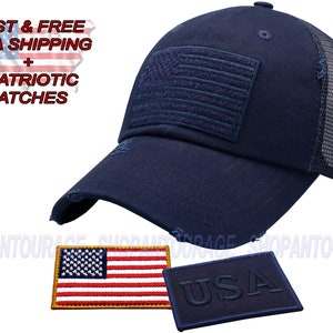 May include: A navy blue trucker hat with a distressed brim and a mesh back. The hat features a navy blue embroidered American flag patch on the front. The hat comes with two patches: a small American flag patch and a larger patch with the word "USA" embroidered in navy blue.