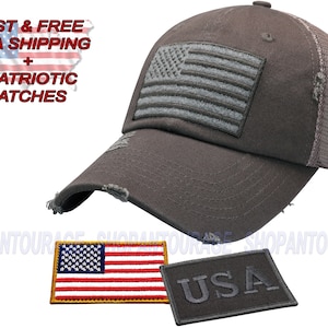 Pode incluir: Boné de caminhoneiro cinza desbotado com uma bandeira americana bordada em cinza na frente. O boné tem uma parte de trás de malha e um remendo preto "USA" no lado. O boné vem com dois remendos adicionais: um pequeno remendo de bandeira americana e um remendo preto "USA".