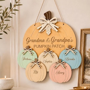 May include: A wooden wall hanging shaped like a large yellow pumpkin with the text Grandma & Grandpa's PUMPKIN PATCH. It features five smaller pumpkins in pastel colors, each with a bow and a name: Jackson, Sophia, Brooks, Lily, and Avery.