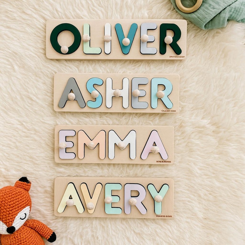 Op de afbeelding: Vier houten naam puzzels met pastelkleurige letters en pinnen. De namen zijn Oliver, Asher, Emma en Avery. Elke puzzel staat op een lichtgekleurde houten basis. De puzzels zijn gerangschikt op een witte, zachte ondergrond.