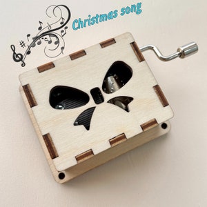 Puede incluir: Una caja de m&uacute;sica de madera con un recorte en forma de lazo y una manivela. La caja de m&uacute;sica reproduce una canci&oacute;n navide&ntilde;a.