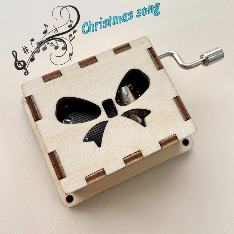 Puede incluir: Una caja de m&uacute;sica de madera con un recorte en forma de lazo y una manivela. La caja de m&uacute;sica reproduce una canci&oacute;n navide&ntilde;a.
