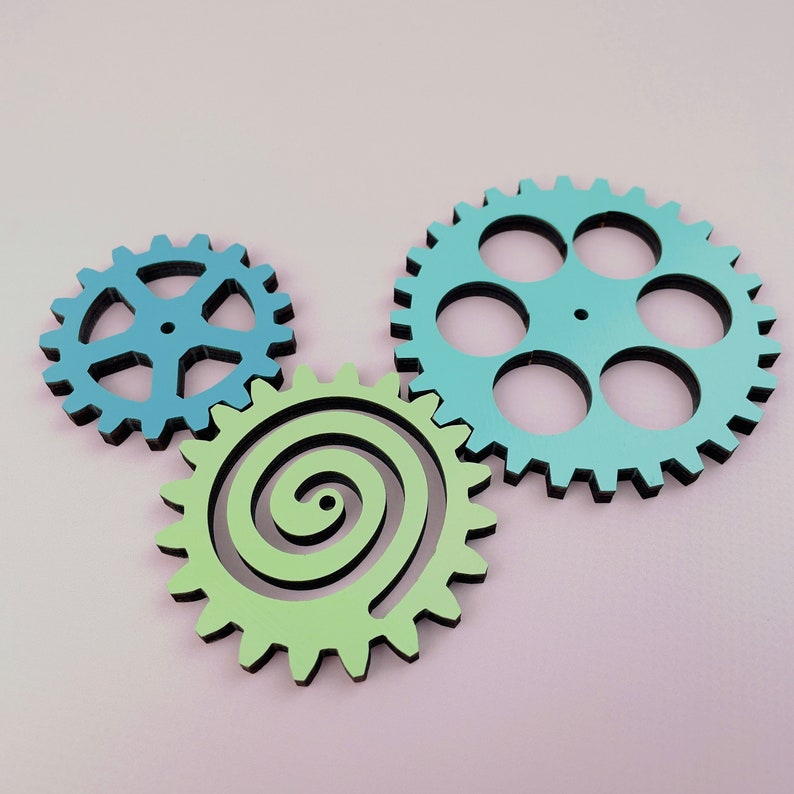 May include: Three wooden gears, one blue, one green, and one light green. The blue gear has six teeth and is the largest. The green gear has a spiral design and is the smallest. The light green gear has a spiral design and is in the middle.