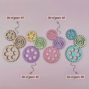 May include: Four sets of colorful wooden gears, each set with a different color scheme. The sets are labeled "Set of gears #1", "Set of gears #2", "Set of gears #3", and "Set of gears #4".