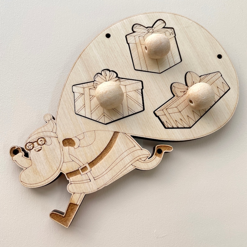 Puede incluir: Juguete de madera con un Pap&aacute; Noel que lleva tres regalos. Los regalos tienen agujeros para clavijas de madera. El juguete est&aacute; hecho de madera natural y tiene un aspecto r&uacute;stico.