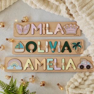 May include: Three wooden personalized puzzle boards with colorful letters spelling out the names Mila, Olivia, and Amelia. Each board features a different design: a butterfly, a sailboat, and a rainbow.