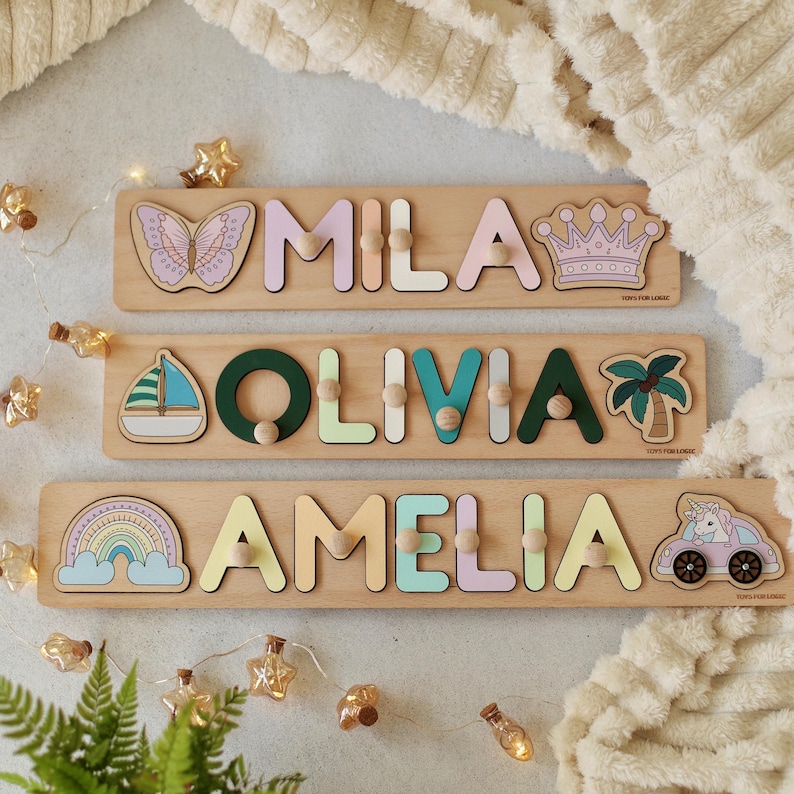 May include: Three wooden personalized puzzle boards with colorful letters spelling out the names Mila, Olivia, and Amelia. Each board features a different design: a butterfly, a sailboat, and a rainbow.