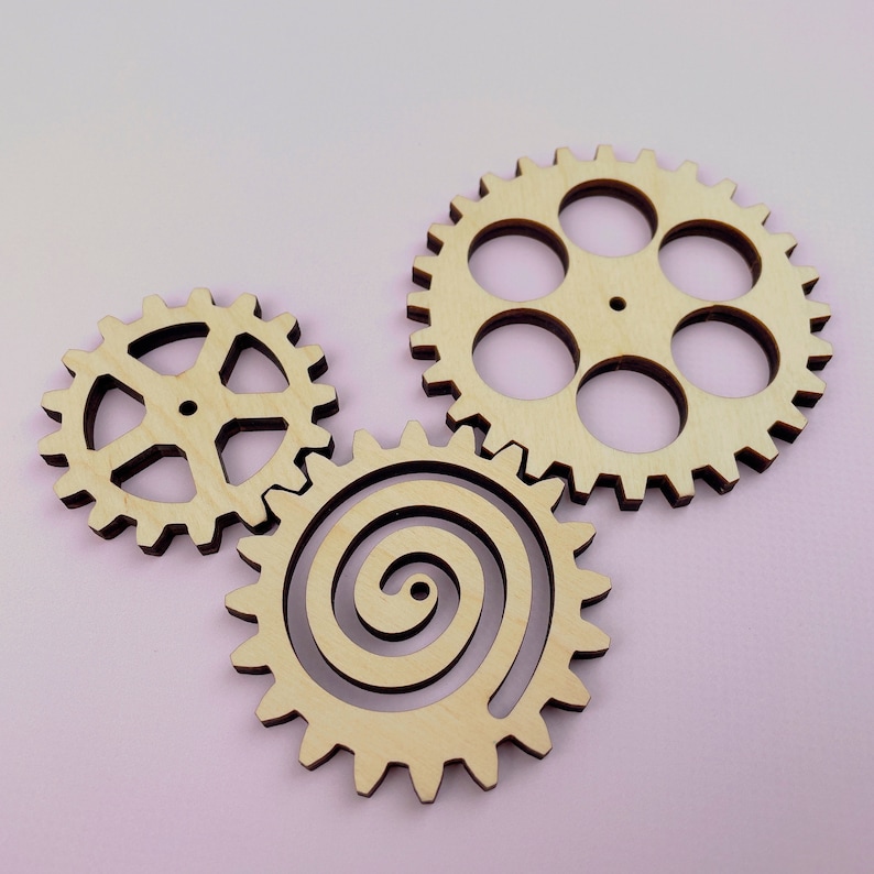 May include: Three wooden gears, one with a spiral design, one with a traditional gear design, and one with a more complex gear design with multiple holes.