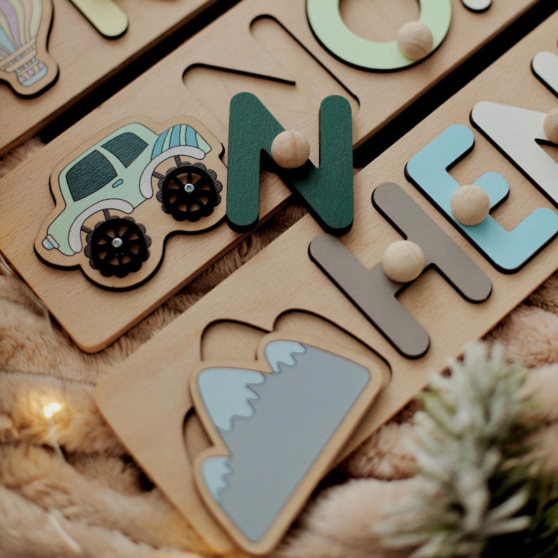 May include: Wooden puzzle with colorful letters spelling out the name "Noah". The puzzle pieces are shaped like a car, mountains, and a hot air balloon. The letters are green, blue, and gray.