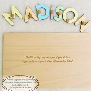 Op de afbeelding: Een houten naam puzzel met de naam "MADISON" in pastelkleuren, met houten pinnen. De puzzel bevat een gegraveerde boodschap op het houten bord: "Mijn liefste, mogen alle jaren van je leven zo gelukkig en gelukkig zijn als je eerste. Fijne eerste verjaardag!"