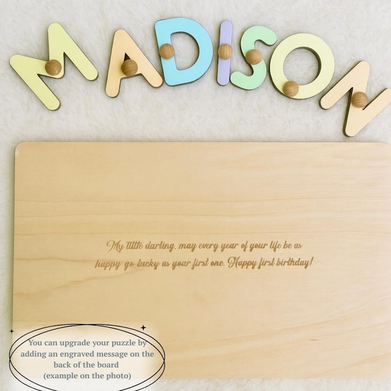 Op de afbeelding: Een houten naam puzzel met de naam "MADISON" in pastelkleuren, met houten pinnen. De puzzel bevat een gegraveerde boodschap op het houten bord: "Mijn liefste, mogen alle jaren van je leven zo gelukkig en gelukkig zijn als je eerste. Fijne eerste verjaardag!"