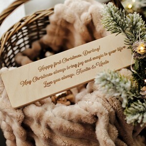 May include: A wooden plaque with a personalized message for a first Christmas. The message reads "Happy first Christmas, Darling! May Christmas always bring joy and magic to your life Love you always, Auntie & Uncle".