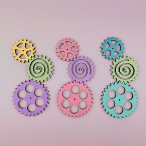 May include: A set of nine colorful wooden gears in various shapes and sizes. The gears are painted in pastel shades of yellow, green, blue, pink, and purple.