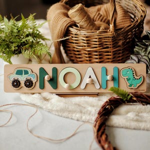 May include: Wooden name puzzle spelling "NOAH" with a car and dinosaur. The letters are in green, white, and teal, with wooden pegs for easy handling. A fun and educational toy for young children.