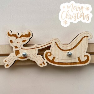 Puede incluir: Renos de madera tirando de un trineo con las palabras "Feliz Navidad" sobre un fondo blanco.