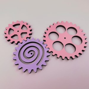 May include: Three wooden gears, one pink with six teeth and five holes, one pink with eight teeth and a spiral design, and one purple with a spiral design.