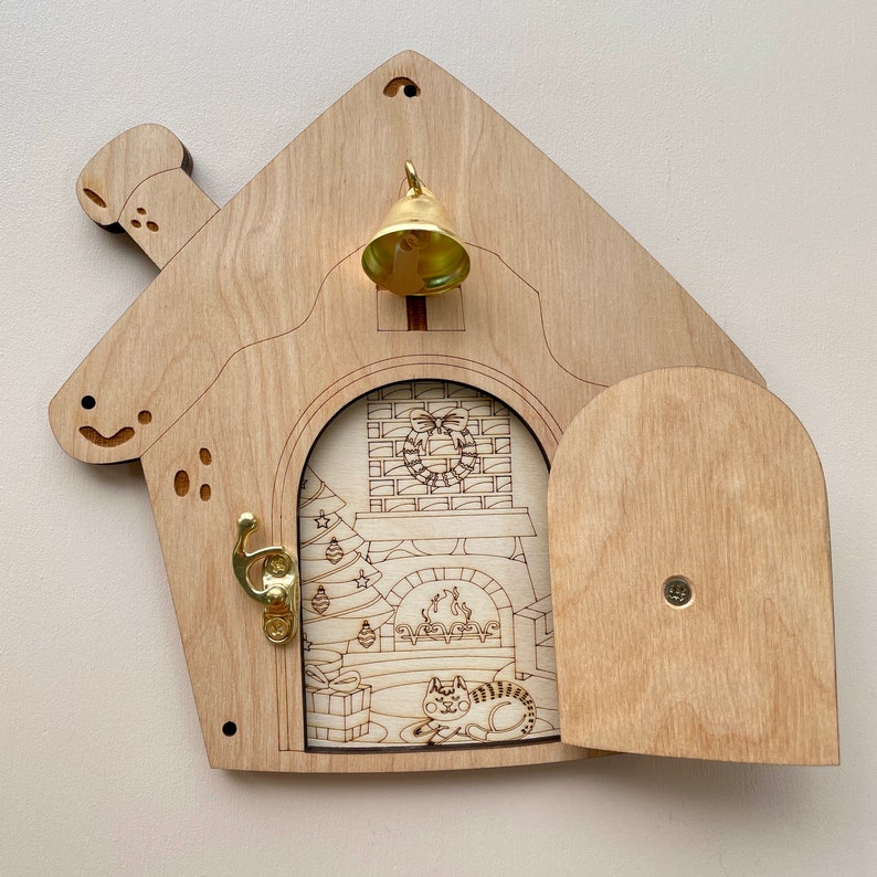 Puede incluir: Una casa de madera de Navidad con un gato dentro, una chimenea, un &aacute;rbol de Navidad y una campana en el techo. La puerta est&aacute; abierta y la casa est&aacute; decorada con una corona.