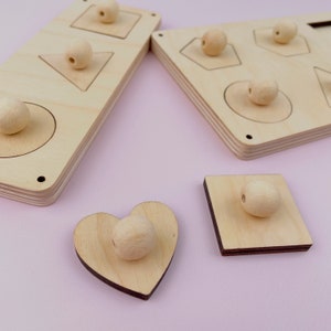 Puede incluir: Juguete de madera con diferentes formas y pomos para que los ni&ntilde;os jueguen. Las formas incluyen un c&iacute;rculo, un cuadrado, un coraz&oacute;n, un tri&aacute;ngulo y un hex&aacute;gono. Los pomos son de madera y est&aacute;n unidos a las formas.
