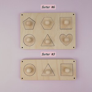 Puede incluir: Dos clasificadores de formas de madera. El clasificador superior tiene seis formas: un pent&aacute;gono, un hex&aacute;gono, un cuadrado, un c&iacute;rculo, un tri&aacute;ngulo y un coraz&oacute;n. El clasificador inferior tiene tres formas: un c&iacute;rculo, un tri&aacute;ngulo y un cuadrado. Cada forma tiene una peque&ntilde;a perilla de madera en el centro.